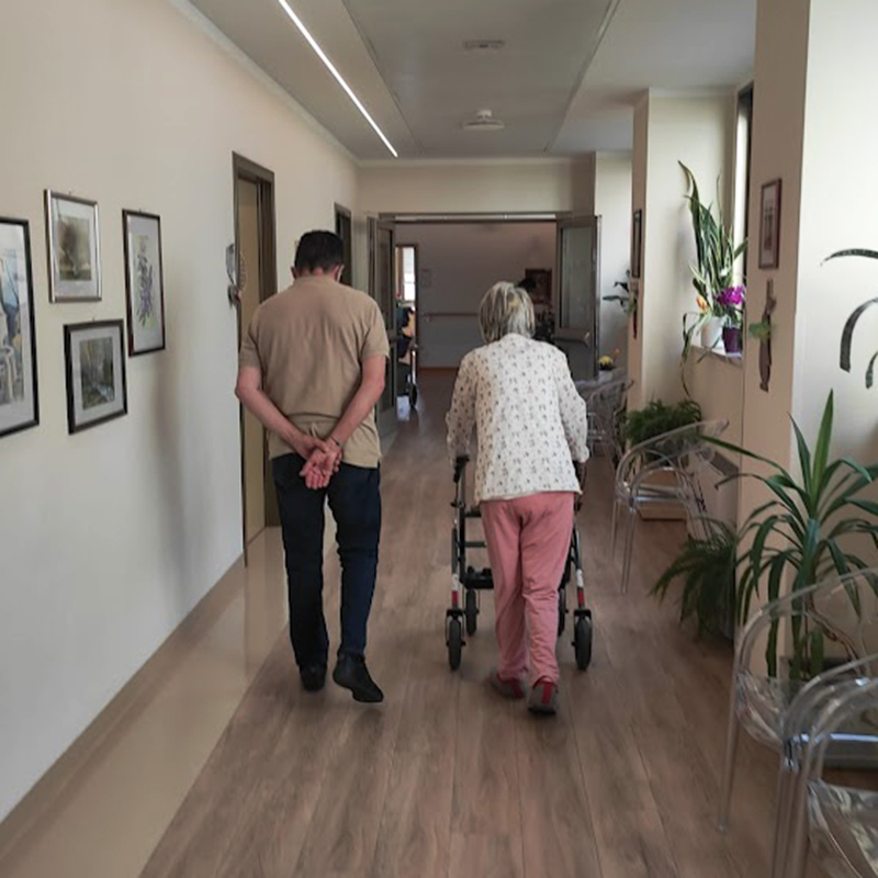 Un volontario accompagna un'ospite con il deambulatore nel corridoio dell'Hospice